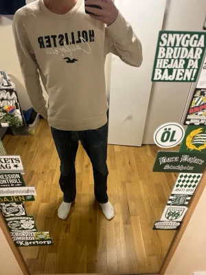 Beige sweatshirt från Hollister - Snygg beige sweatshirt från Hollister med svart och vit logga och texten 'California' på bröstet. Tröjan har rund halsringning och långa ärmar. Perfekt för en avslappnad och stilren look.