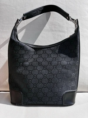 Svart axelväska - Svart handväska i textil med texttryck. Rymlig fodrad insida med öppet sidofack. Bra skick överlag Mått: Bredd 28 cm, höjd 46 cm (med handtag), djup 11.5 cm