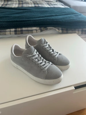 Selected home mockar skor - Snygga grå sneakers med ovandel i mocka-liknande material och matchande grå skosnören. Klassisk låg modell med vit sula som passar till det mesta. Perfekta för dig som gillar stilrena och enkla skor.