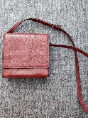 Brun axelväska i läder, Wera - Säljer en snygg brun axelväska från Wera av läder. Väskan har en fyrkantig form, justerbar axelrem och stilren design med guldfärgad logga framtill. Perfekt för dig som gillar trendiga accessoarer med lite edge.