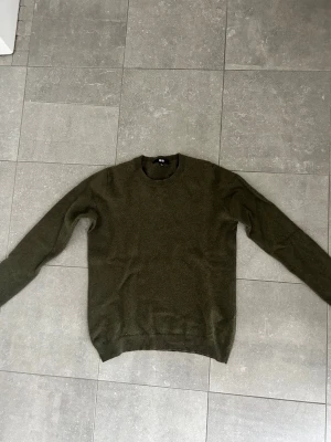 Olivgrön stickad tröja - En enkel och stilren olivgrön stickad tröja med rund halsringning och långa ärmar. Tröjan har ribbade muddar vid ärmslut och nederkant, perfekt för lager på lager under kyliga dagar. Vid frågor eller funderingar är de bara att höra av sig!