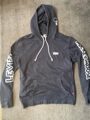 Levi’s x Disney Hoodie - Snygg svart huvtröja från Levi’s i samarbete med Disney/Mickey Mouse.  ✅ “Levi’s”-tryck i vitt på vänster ärm ✅ “Mickey Mouse”-tryck i vitt på höger ärm ✅ Broderad Mickey Mouse-siluett på huvan ✅ Klassisk Levi’s-logga (röd tab) på bröstet ✅ Vita dragsnören i huvan ✅ Bekväm, tjock bomullskvalitet – perfekt för vardag och skön avslappnad stil  Skick: Mycket bra Storlek: L  Fri från fläckar och hål – bekväm och sval hoodie som passar till det mesta. Fråga gärna om fler bilder eller mått!