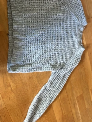Ljusgrå stickad tröja XS - Ljusgrå stickad tröja med grovstickat mönster och ribbade muddar vid ärmslut och nederkant. Tröjan har rund halsringning och är perfekt för kyliga dagar. Enkel och stilren design som passar till det mesta.