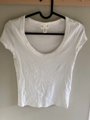 Vit ribbad croppad topp - Säljer en vit ribbad croppad topp med korta ärmar och rundad, djup urringning. Perfekt att matcha med jeans eller kjol för en enkel och fräsch look. Materialet är mjukt och stretchigt för skön passform.