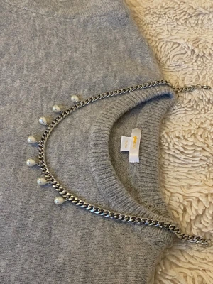 Silverfärgat halsband med pärlor - Snyggt halsband i silverfärgad rostfritt med kedja och hängande vita pärlor. Kedjan har en chunky känsla och pärlorna ger en elegant touch. Perfekt för att lyfta vilken outfit som helst med lite extra stil.