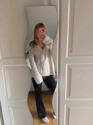 Beige oversized stickad tröja - Mysig beige stickad tröja med v-ringning och kabelstickat mönster. Tröjan har en oversized passform, långa ärmar och ribbade muddar. Perfekt för lager på lager och chill dagar.