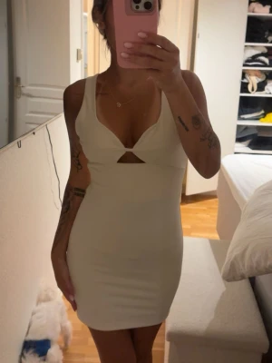 Benvit kort klänning med cut-out - Säljer en ben vit, tight kort klänning med breda axelband och snygg cut-out detalj framtill. Klänningen har en kroppsnära passform och är perfekt för dig som vill ha en enkel men trendig look.