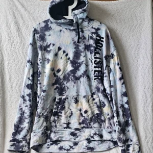 Tie-dye hoodie från Hollister XL - Säljer en snygg tie-dye hoodie från Hollister i storlek XL. Hoodien har svart och vit batikmönster, stor magficka och justerbar huva med snörning. Hollister-logga tryckt längs bröstet. Perfekt för dig som gillar avslappnad stil.