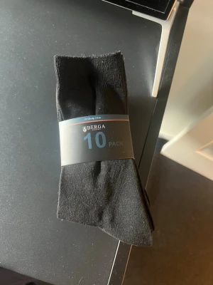 Svarta strumpor 10-pack från Berga helt oanvända kvar i förpackningen  - Säljer ett 10-pack svarta strumpor från Berga i storlek 39/42. Strumporna är klassiskt enkla och passar perfekt till vardags. De är tillverkade i ett mjukt och bekvämt material som sitter skönt på foten. Säljer då dom är fel storlek. 