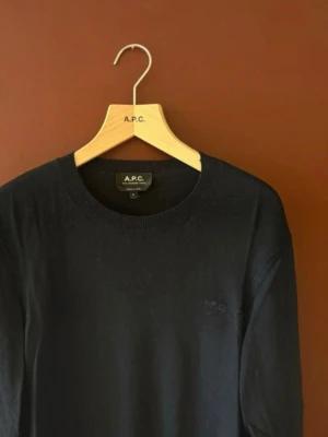 Svart tröja från A.P.C. - Snygg svart långärmad tröja från A.P.C. i tunnare material med rund halsringning och diskret broderad logga på bröstet. Perfekt för en clean och stilren look. Klassisk passform och ribbade muddar vid ärmslut och nederkant. S men skulle säga att den passar mer xs 