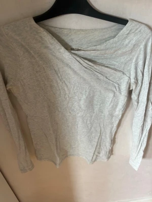Ljusgrå asymmetrisk topp med lång ärm - Snygg ljusgrå asymmetrisk topp med lång ärm och v-ringad hals. Toppen har en enkel och stilren design som passar perfekt till jeans eller kjol. Tillverkad i mjukt bomullsmaterial för en bekväm känsla hela dagen 💗