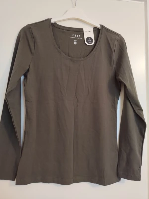 Olivgrön långärmad topp - En stilren olivgrön långärmad topp med rund halsringning. Toppen är i mjuk bomull och har en enkel, klassisk design som passar till många olika outfits.