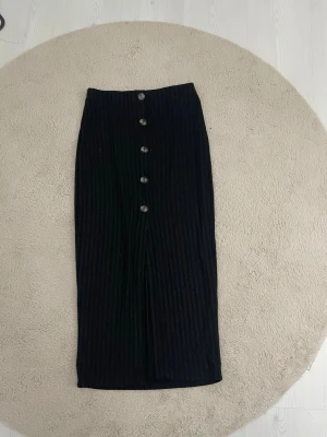 Svart ribbad långkjol från SHEIN - Stilren svart långkjol från SHEIN med ribbad struktur och knappar framtill. Kjolen har en rak passform och en liten slits framtill för extra rörelsefrihet. Perfekt att matcha med en enkel topp eller stickad tröja.