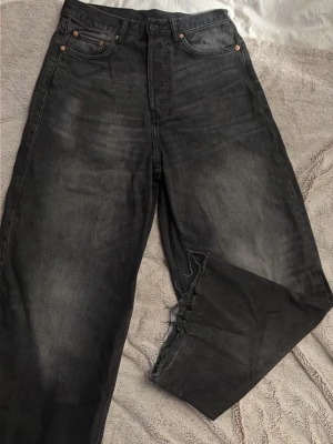 Svarta raka weekday jeans med rå kant - Säljer ett par svarta jeans från weekday med rak passform och snyggt slitna detaljer. Jeansen har hög midja, fransig kant nedtill på benen för en edgy look. Materialet är klassisk denim i bomull. Perfekta för dig som gillar en avslappnad och trendig stil. Storleken är W27 och L34.
