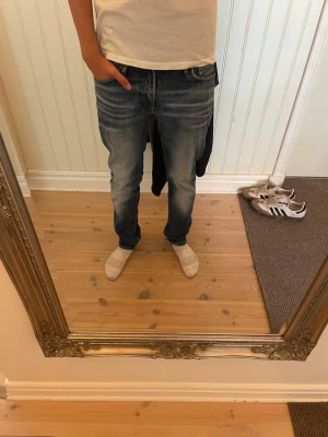 Blå slim fit jeans med slitningar - Säljer ett par blå slim fit jeans med snygga slitningar och tvättade detaljer. Jeansen har klassisk femficksmodell, normal midja och raka ben. Perfekta för en avslappnad och trendig stil.