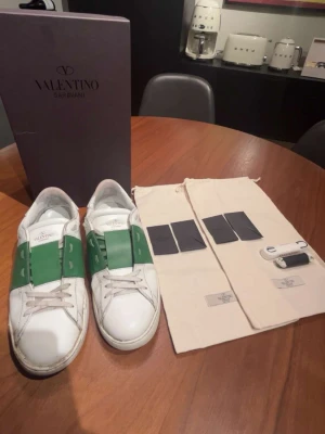 Valentino Garavani vita sneakers grönt band - Tjena säljer nu ett par Valentino open med en unik grön färg. Köpte skorna nya av brorsan då storlek inte passade han. Nya snören följer med samt boxen och de andra på sista bilden. Storleken är 44,5. Fråga vid minsta fundering 💭 