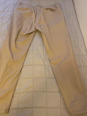 Beiga chinos med raka ben - Stilrena beiga chinos med raka ben och klassisk passform. Byxorna har två bakfickor med knapp, bälteshällor och stängs med knapp och dragkedja. Tillverkade i mjukt bomullstyg som ger en clean och avslappnad look.