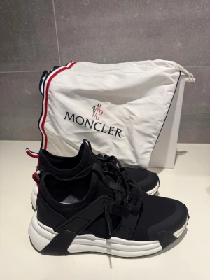 Svarta sneakers från Moncler - Sneakers från Moncler i storlek 41. Modell ”Lunarove”. Alla tillbehör medföljer (orginallåda, dustbag, qr-kod för äkthetsintyg). Skorna är använda några gånger så lite tecken på användning förekommer, de mesta går att tvätta bort. Se bilderna, begär gärna fler bilder vid intresse! 