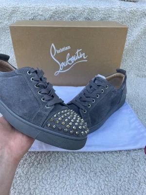 Christian Louboutin Louis Junior Spikes Suede (Grey) - Säljer ett par extremt stilrena Christian Louboutin Louis Junior Spikes Low-Top i mörkgrå mocka. Skorna är i mycket gott skick och väl omhändertagna med en riktigt fräsch ovandel och fina sulor. De levereras helt kompletta med originalkartong, dustbag, köpbevis från Harrods samt extra tillbehör. Storlek:  EU 41,5, men skulle säga passar ganska mycket större storlekar också. Tveka inte att höra av dig vid frågor eller om du vill ha fler bilder — skickas naturligtvis spårbart och säkert! Skorna ha