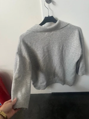 Grå stickad tröja med krage - Mysig grå stickad tröja från H&M med bred krage och v-ringad öppning framtill. Tröjan är enkel att matcha och passar till nästan alla årstider 