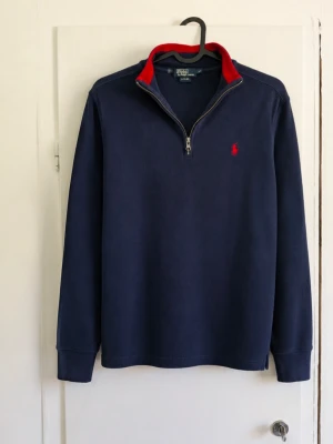 Polo Ralph Lauren quarter zip marinblå – M (10–12) 🔴🔵 - Klassisk Polo by Ralph Lauren quarter zip i marinblått med snygga röda detaljer. Röd insida i kragen och den ikoniska broderade Polo-loggan på bröstet. • Storlek M (10–12), barn/ungdom • Marinblå med röda detaljer • Quarter zip / half zip • Broderad röd Polo-logga • Ribbad krage och ärmslut • Klassisk äldre Polo by Ralph Lauren-modell • Fint begagnat skick utan defekter förutom att den är lite färg blekt!😁 Snygg både över skjorta och som vanlig tröja. Skriv gärna vid frågor eller för mått 📦