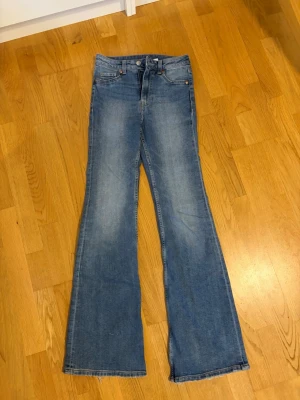 Blå utsvängda jeans med hög midja - Snygga blå jeans med utsvängda ben och hög midja. Klassisk femficksmodell i mjukt denimtyg. Perfekta för dig som gillar en retroinspirerad look och vill ha ett par jeans som sticker ut lite extra.