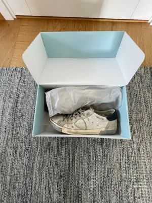 Phillipe Modell - Säljer ett par vita sneakers i mocka med lågt skaft och silver detaljer vid hälen. Skorna har en klassisk siluett, snörning framtill och slitna detaljer för en avslappnad look. Passar perfekt till streetwear och casual outfits.
