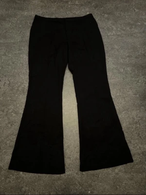 Svarta kostymbyxor  - Säljer ett par svarta kostym byxor med utsvängda ben. Byxorna har en enkel design utan synliga fickor eller detaljer och är tillverkade i ett mjukt, stretchigt material som sitter skönt på kroppen. Perfekta för dig som gillar en stilren och trendig look.