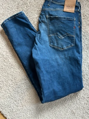 Replay anbass hyperflex blå - Säljer ett par klassiska blå replay anbass hyperxlex. Jeansen är i storlek 32 och slim fit. Materialet är mjukt denim som ger en avslappnad. Jeansen har ett slitage, se bild 6.