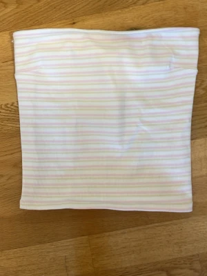 Randig bandeau tubtopp från Gina Tricot - Säljer en söt bandeau tubtopp från Gina Tricot i vitt med tunna pastellrosa och beige ränder. Toppen är ribbad och axelbandslös, perfekt för sommardagar eller festivaler. Superenkel att matcha med jeans eller kjol!