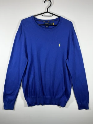 Polo Ralph Lauren Pima Cotton Tröja Blå – Slim Fit L - Klassisk blå stickad tröja från Polo Ralph Lauren med gul broderad Pony-logga på bröstet.  • Storlek: L • Passform: Slim Fit • Pima Cotton • Blå med gul broderad logga • Rund hals • Fint begagnat skick 