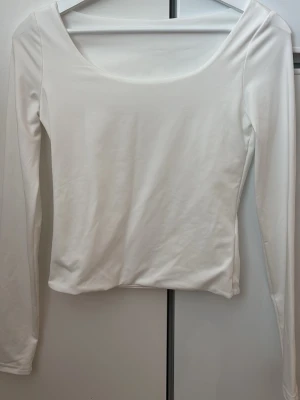 Vit långärmad topp med rund hals - En stilren vit långärmad topp med rundad halsringning. Toppen har en tight passform och är tillverkad i ett mjukt, stretchigt material som känns skönt mot huden. Perfekt att matcha med jeans eller kjol för en clean look.