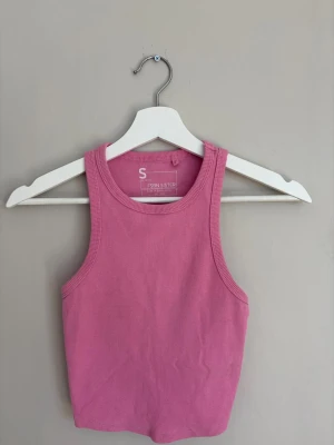 Rosa ribbad linnetopp - Säljer en rosa ribbad linnetopp med rund halsringning och croppad passform. Perfekt för varma dagar och enkel att styla med jeans eller kjol. Materialet är mjukt och stretchigt för extra komfort.