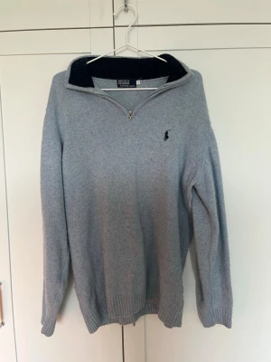 Ljusblå stickad tröja Polo Ralph Lauren - Ljusblå stickad tröja från Polo Ralph Lauren med halv dragkedja och mörkblå ribbad krage. Klassisk broderad logga på bröstet. Tröjan har långa ärmar och ribbade muddar vid ärmslut och nederkant. Perfekt för lager på lager och snygg till jeans.