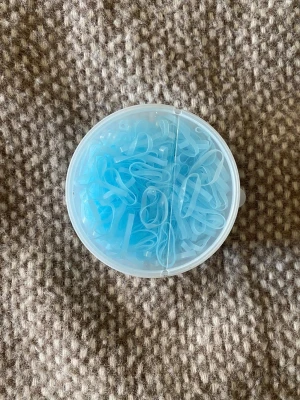 Blåa små hårsnoddar i ask till häst - En rund plastask fylld med små, tunna hårsnoddar i ljusblått till häst. Perfekta för att fixa detaljerade frisyrer eller flätor. Snoddarna är gjorda av elastiskt material och är genomskinligt blåa.