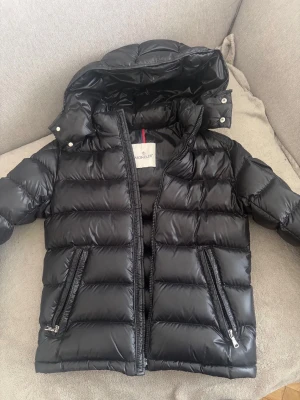 new maya jacket moncler  -  stlrk 152 men passar på 158 också( kvitto finns)  Äkta new maya jacket  svart  från Moncler med glansig finish, huva och två dragkedjefickor framtill. Klassisk Moncler-logga på ärmen och quiltad design. Perfekt för kalla vinterdagar och riktigt varm tack vare dunfyllningen.