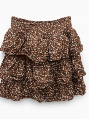 Brun blommig volangkjol - Söt brun kortkjol med små vita blommor och flera volanglager. Kjolen har bred resår i midjan för skön passform och ett luftigt, flowigt fall. Perfekt för dig som gillar romantisk och avslappnad stil.