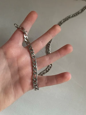 Silverfärgat kedjehalsband - Säljer ett stilrent halsband i silverfärgad metall med platta, breda länkar. Kedjan har ett klassiskt karbinlås och passar perfekt för dig som gillar en clean och enkel look. Halsbandet är tidlöst och lätt att matcha med olika outfits.