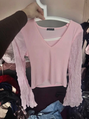 Ljusrosa topp med spetsärmar - Supersöt ljusrosa topp från little sister’s med v-ringning och långa spetsärmar. Toppen har en figurnära passform och är perfekt för dig som vill ha en romantisk och trendig look. Ärmarna är genomskinliga och ger en extra detalj till outfiten.Storlek: M (Upplevs som något tajt i passformen, så den passar även dig som vanligtvis bär storlek S).