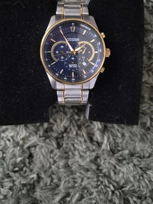 Citizen herrklocka i silver och guld - Stilren Citizen herrklocka med blå urtavla, silverfärgad länk och gulddetaljer. Klockan har flera små urtavlor, tachymeter och tydliga indexmarkeringar. Perfekt accessoar för dig som vill ha en klassisk men modern look.