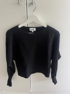 Svart ribbad stickad tröja ONLY - Säljer en svart ribbad stickad tröja från ONLY. Tröjan har rund halsringning, långa ärmar och breda muddar vid ärmsluten. Perfekt basplagg till garderoben och enkel att styla med olika outfits.