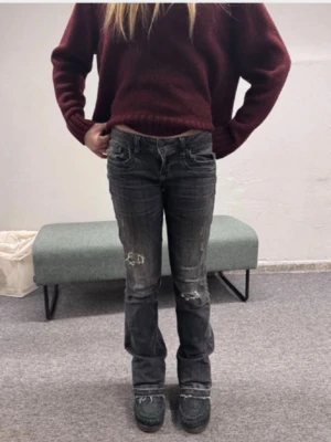 Svarta slitna bootcut jeans - Säljer ett par svarta bootcut jeans med slitningar och hål på benen. Jeansen har låg midja och klassisk femficksmodell. Materialet är denim med en tvättad look och råa detaljer vid benslut. Perfekta för en avslappnad och trendig stil.
