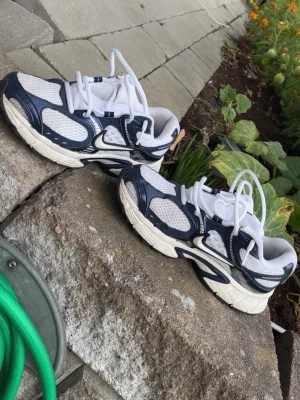 Vita och marinblå sneakers - Snygga sneakers i vitt och marinblått med meshpaneler och detaljer i syntet. Skorna har en sportig look med tjock sula och vita skosnören. Perfekta för dig som gillar retrostil och streetwear.