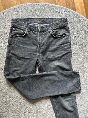 Grå jeans från Nudie Jeans - Säljer ett par grå jeans från Nudie Jeans med klassisk femficksmodell och raka ben. Jeansen har en tvättad look och är tillverkade i denim. Perfekta för dig som gillar en avslappnad och stilren stil.