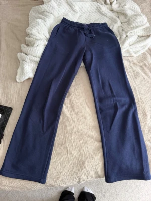 Mörkblå mjukisbyxor med raka ben - Mörkblå mjukisbyxor med raka ben och resår i midjan samt dragsko. Byxorna har sidofickor och är gjorda i ett mjukt, bekvämt material som känns skönt mot huden. Perfekta för chill dagar hemma eller när du vill vara extra comfy. Smutsiga (se bilder) går nog bort i tvätten här ej provat. 