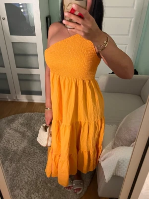 Orange oneshoulder långklänning - Säljer en orange oneshoulder klänning. Klänningen har volangdetaljer och är tillverkad i ett lätt, luftigt tyg som passar perfekt för varma dagar. Har använt en gång men den är som ny.