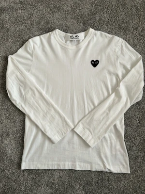 CDG Play Longsleeve - Säljer nu denna vita långärmade tröjan från Comme des garçons play. Den har använts fåtal gånger då den satt ganska tajt på mig. Tröjan har väldigt små fläckar på ryggen och bakom armen som syns inte alls, men är ändå inkluderade de sista 2 bilderna. Hör av gärna vid intresse🙌
