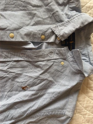 Ljusblå skjorta från Ralph Lauren - Klassisk ljusblå skjorta från Ralph Lauren med broderad logga på bröstet. Skjortan har knappar framtill och en snygg krage. Tillverkad i mjuk bomull som känns skön mot huden. 