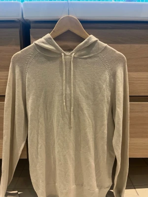 Beige tunn hoodie med huva - En stilren beige hoodie med huva och dragsnören. Tillverkad i ett tunt, mjukt material som känns skönt mot huden. Hoodien har långa ärmar och ribbade muddar vid ärmslut och nederkant. Perfekt för en avslappnad look.