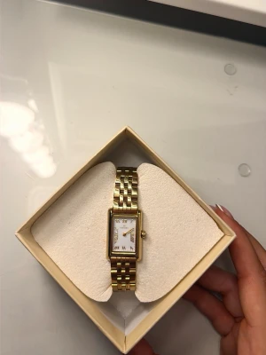 Mockberg klocka - Stilren guldfärgad armbandsklocka med rektangulärt ur och vit urtavla. Från Mockberg. 